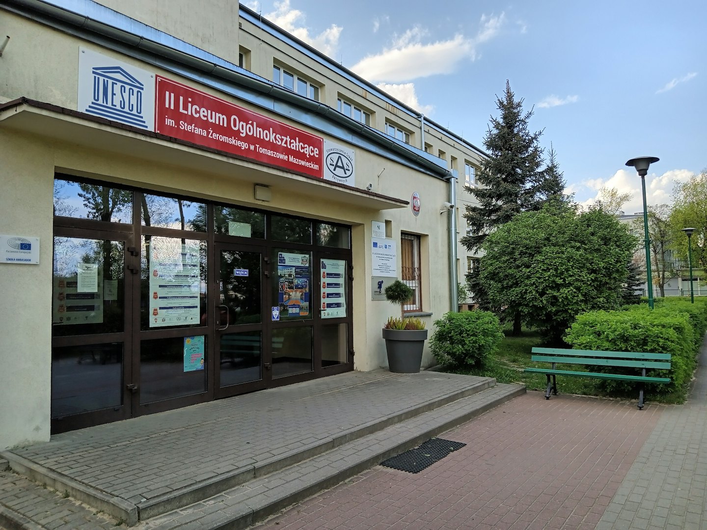 Dwupiętrowe wejście do szkoły ze szklanymi drzwiami i drewnianą ławką.
